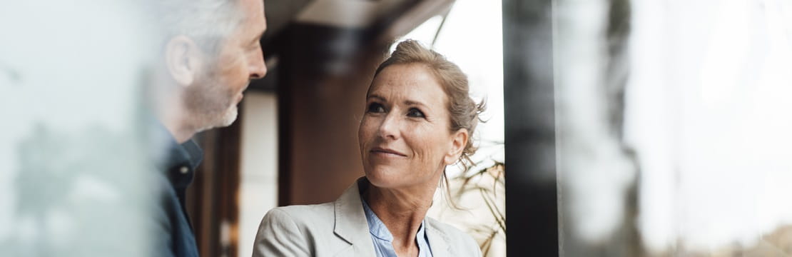 Smiling businesswoman with businessman in cafe seen through glass